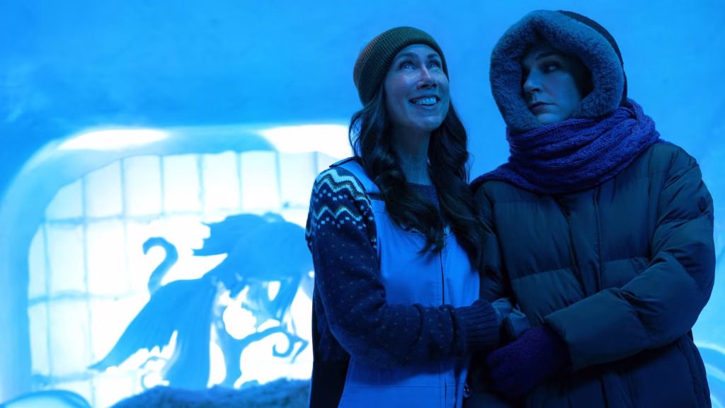 Two women dressed in winter clothing stand together in a blue-lit icy setting in a scene from Pluribus.