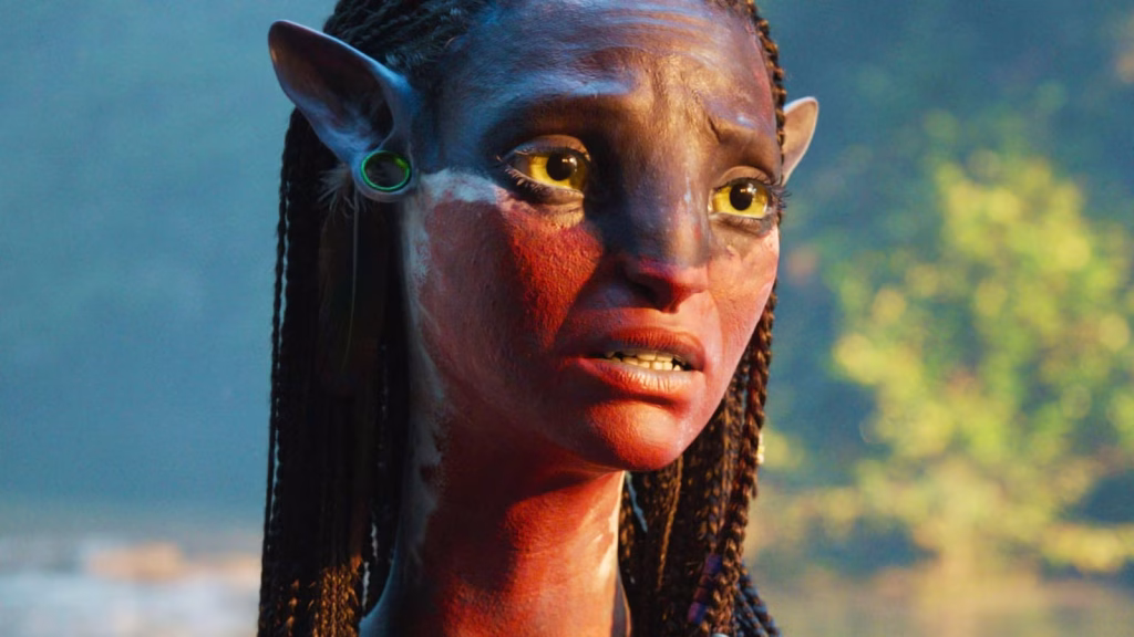 Close-up of Neytiri, a blue Na’vi woman with braided hair and golden eyes, looking worried with her mouth slightly open in warm sunlight.