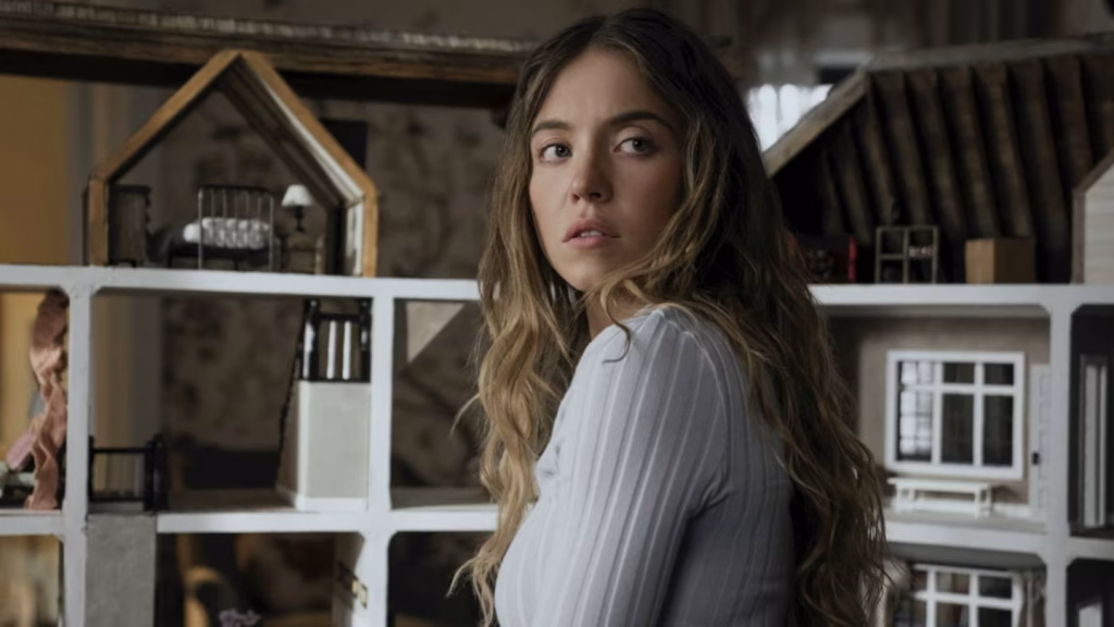 Sydney Sweeney as Millie Calloway looks over her shoulder beside a detailed dollhouse model inside the Winchester home, tense and watchful.