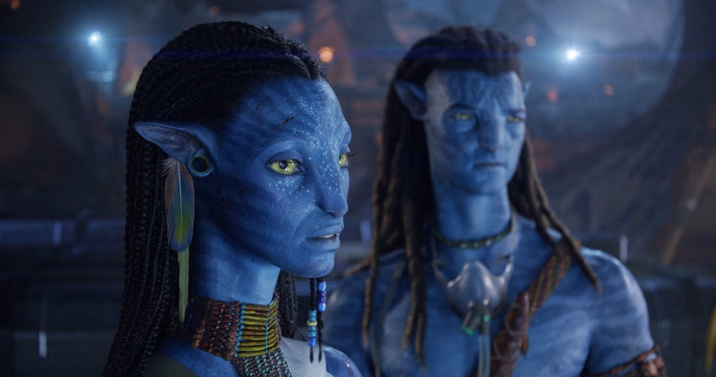Neytiri is shown in close-up with Jake Sully blurred in the background, both standing in a smoky scene lit by distant fires and scattered glowing embers.