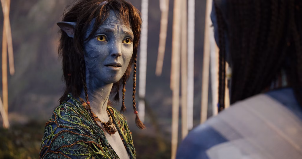 Kiri, a young Na’vi with short hair, looks worried as she speaks to another Na’vi seen from behind in a softly lit outdoor setting.