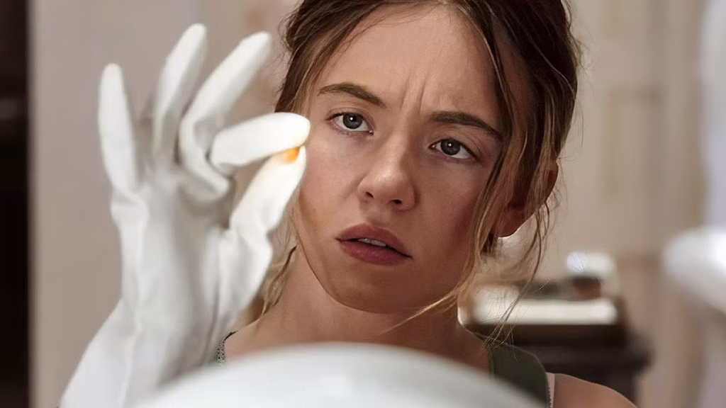 Sydney Sweeney’s character Millie wears white gloves and studies a small object between her fingers with a tense, focused expression.