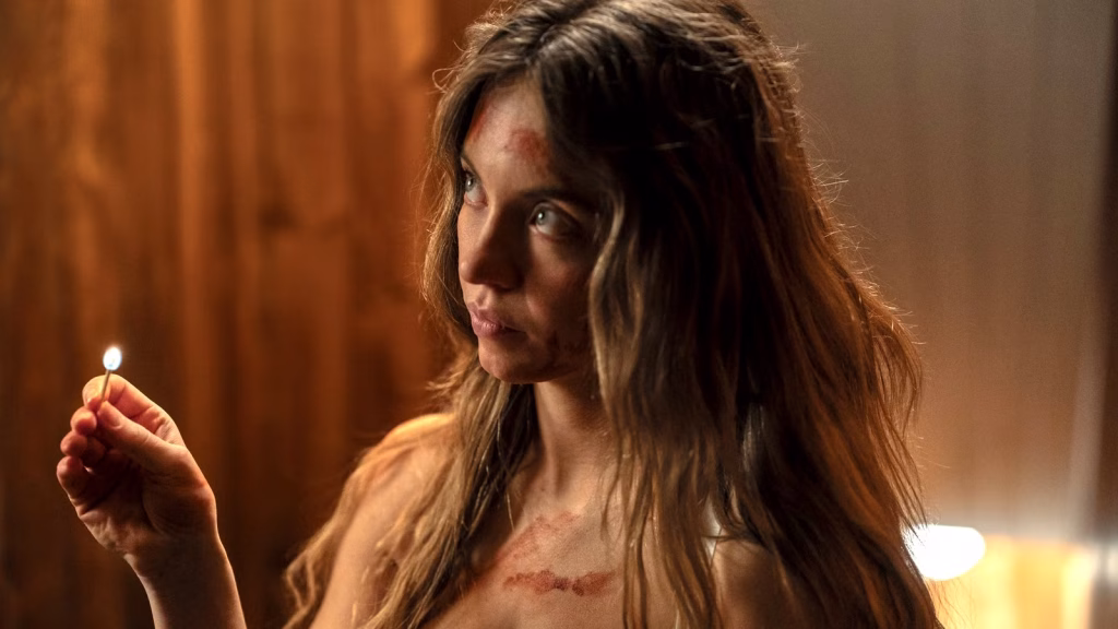 Sydney Sweeney as Millie stares intensely while holding a lit match, with blood visible on her face and clothing.