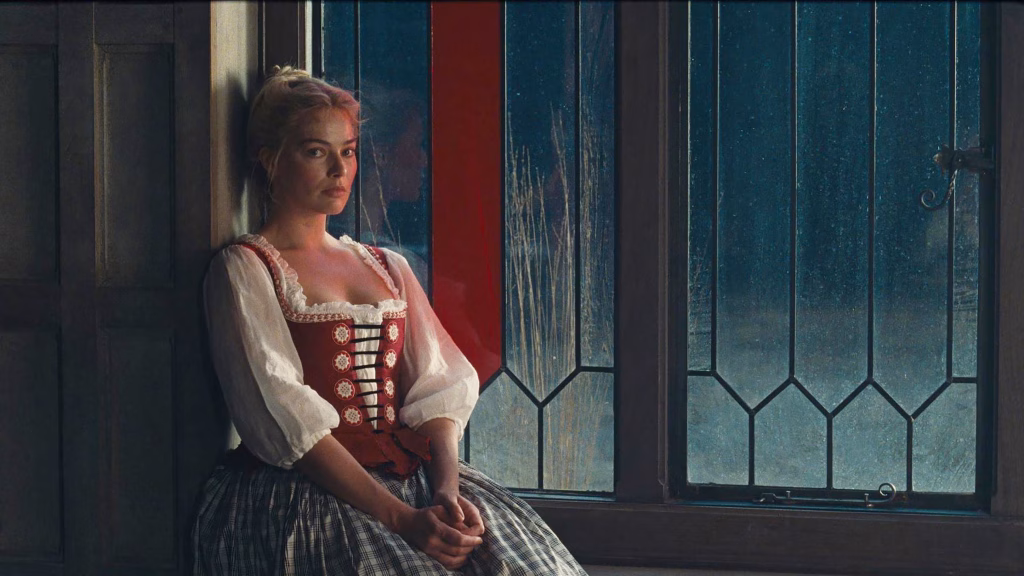 Margot Robbie as Catherine Earnshaw sits beside a stained-glass window in period costume, looking ahead with a calm but guarded expression.
