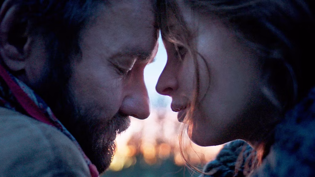 Joel Edgerton and Felicity Jones lean close together in a softly lit close-up scene from Train Dreams.