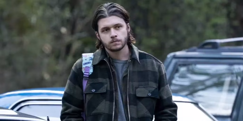 Nick Robinson as Sean stands outdoors near parked cars in Maid.