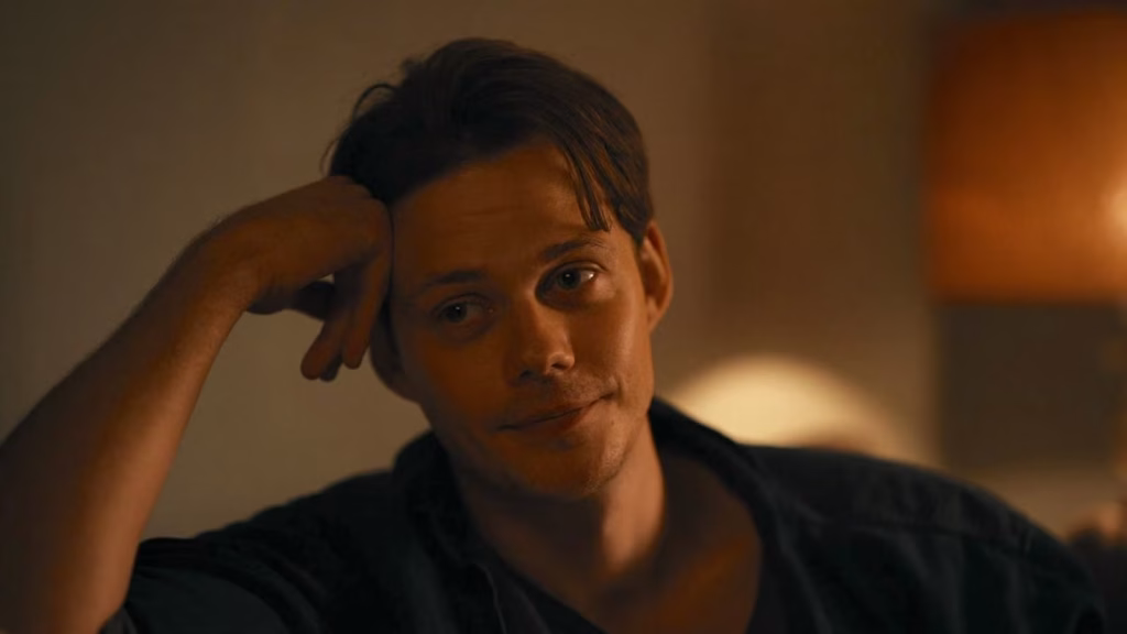 Bill Skarsgård as Keith sits in a dimly lit room in Barbarian.