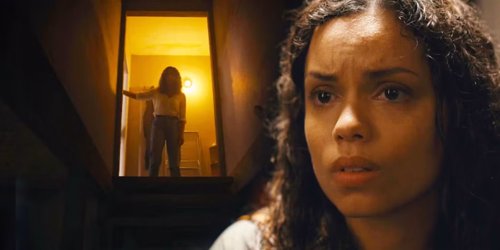 Tess from Barbarian looks worried inside a dim house as a figure stands in a lit doorway.