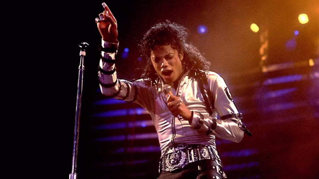 Michael Jackson sings onstage under concert lights with one arm raised.
