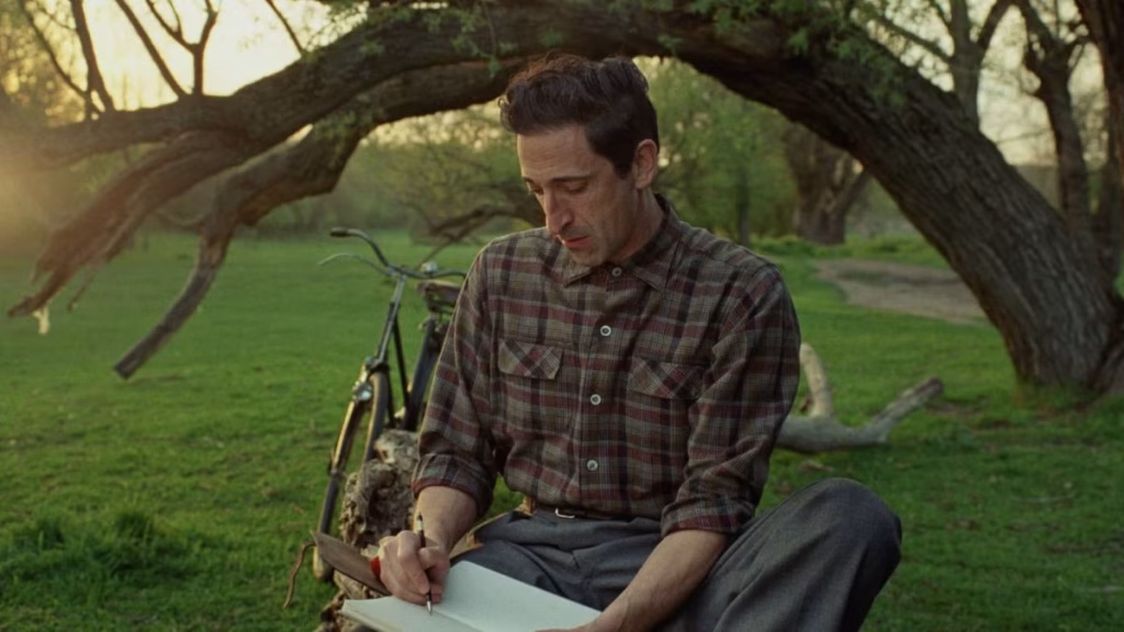 László Tóth sits under a tree and writes in a notebook beside a bicycle.