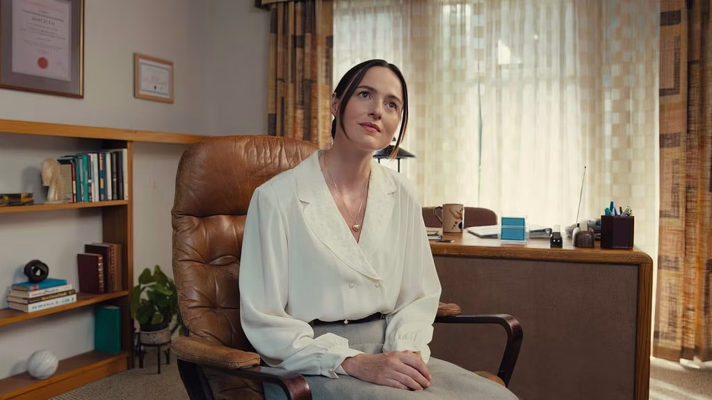 Renate in a white blouse sits in a leather chair inside a softly lit office.