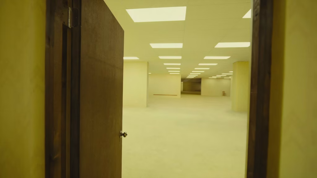 Open doorway leading into an empty yellow Backrooms room with fluorescent lights.