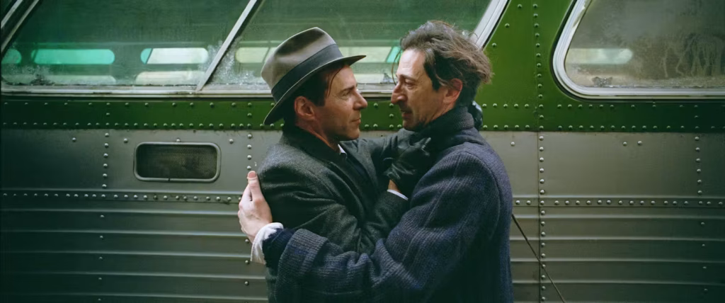 László Tóth and Harrison Lee Van Buren embrace beside a train in The Brutalist.