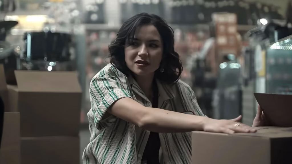 Nikki leans across stacked boxes inside the record store in Obsession.
