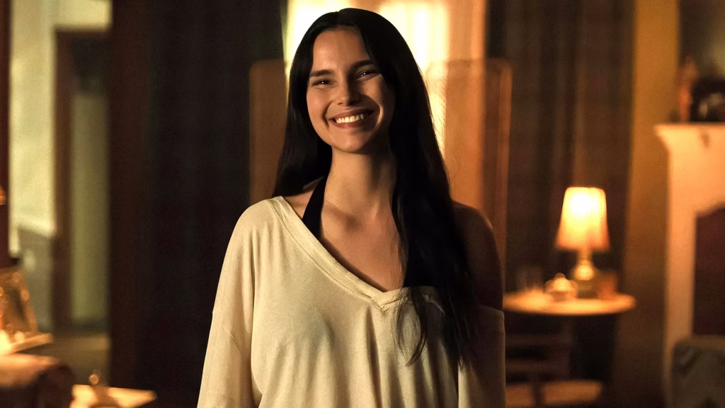 Inde Navarrette as Nikki smiles in a warmly lit room in Obsession.