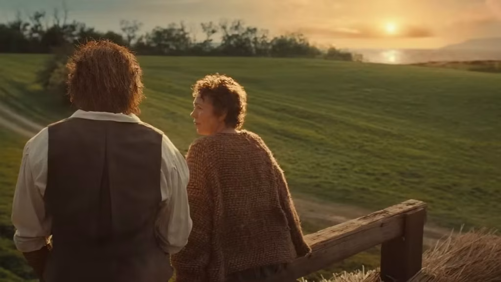 The Fisherwoman and her Wicker Husband look across green fields toward a coastal sunset.