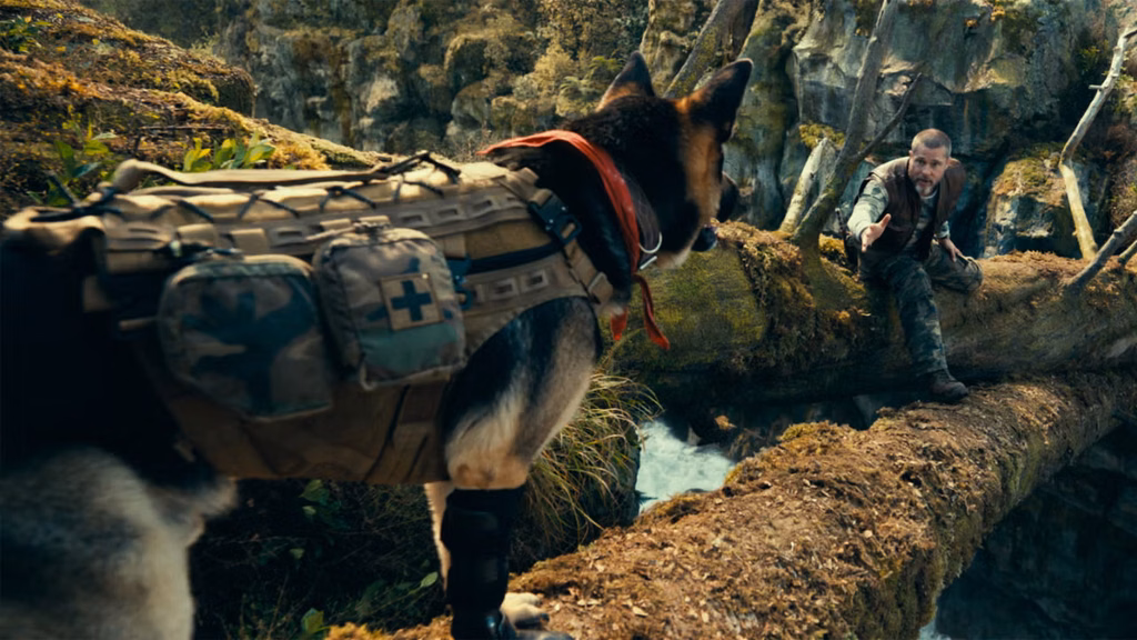 Brad Pitt reaches towards a German Shepherd in a tactical harness on a moss-covered log above rushing water.